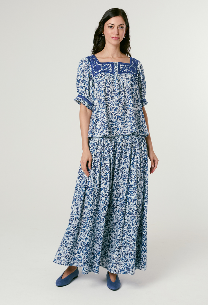 Woman wearing a blue floral bouse and skrit on a white background