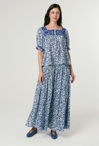 Woman wearing a blue floral bouse and skrit on a white background