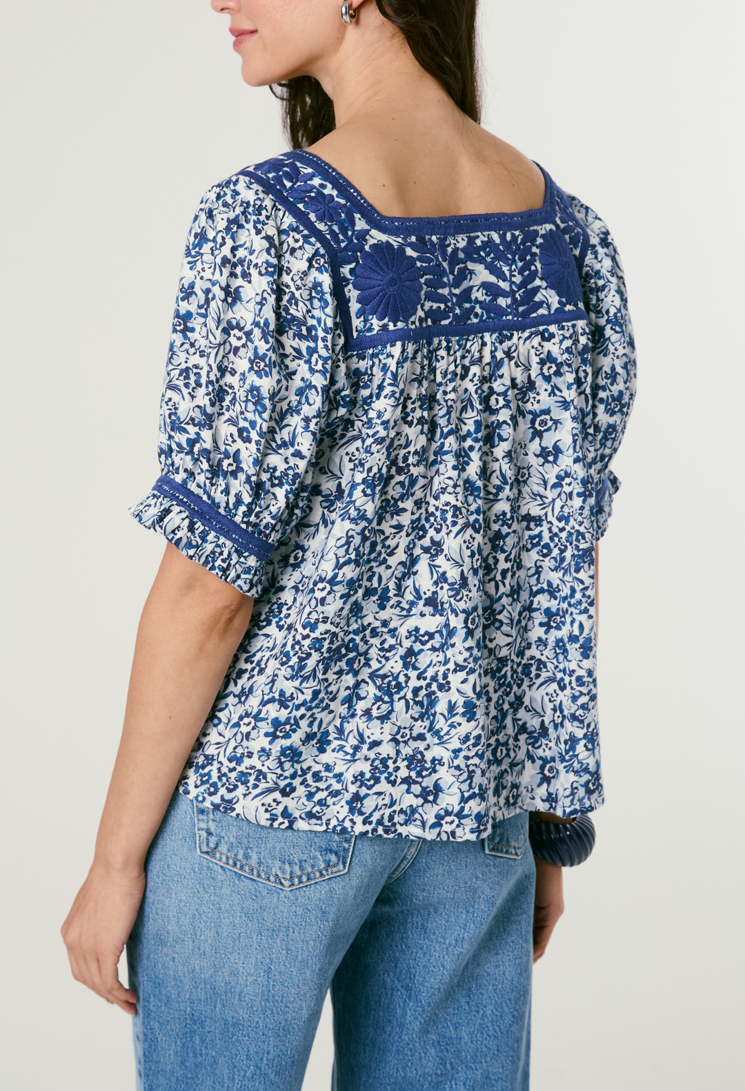 Woman wearing a blue floral blouse with embroidered details on a plain background
