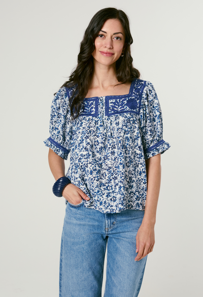 Woman wearing a blue floral blouse and jeans on a plain background