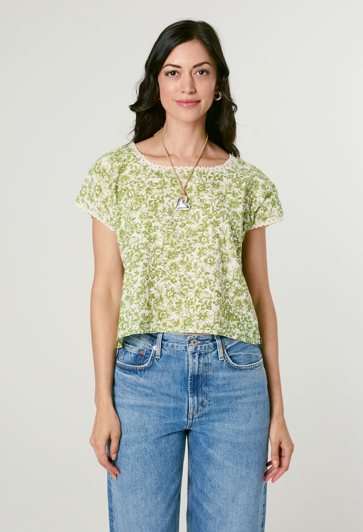 Woman wearing a green floral top and blue jeans against a plain background